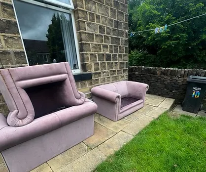 Old sofa and armchair left on a paved area beside a stone house