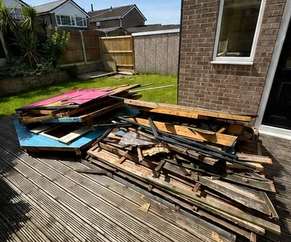 Broken decking boards and garden waste stacked on a lawn beside a house