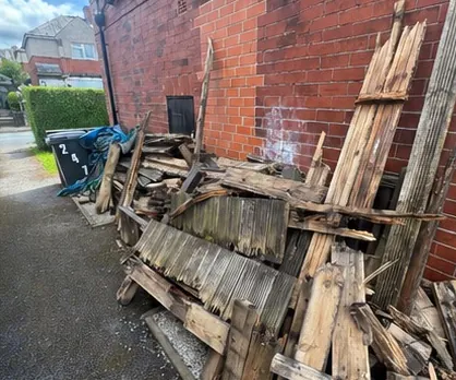 Stack of broken timber, pallets and builders waste dumped against a brick wall
